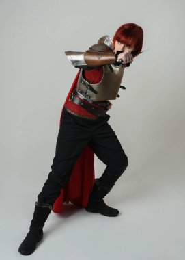 Savaşçı kadın şövalyenin tam boy fantezi portresi, tarihi ortaçağ çelik zırh kostümü giyen bir model, kırmızı peri masalı pelerini. Ayakta durma pozu, izole edilmiş stüdyo arka planı.