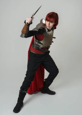 Savaşçı kadın şövalyenin tam boy fantezi portresi, tarihi ortaçağ çelik zırh kostümü giyen bir model, kırmızı peri masalı pelerini. Ayakta durma pozu, izole edilmiş stüdyo arka planı.