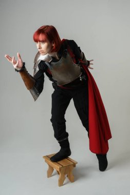 Savaşçı kadın şövalyenin tam boy fantezi portresi, tarihi ortaçağ çelik zırh kostümü giyen bir model, kırmızı peri masalı pelerini. Ayakta durma pozu, izole edilmiş stüdyo arka planı.