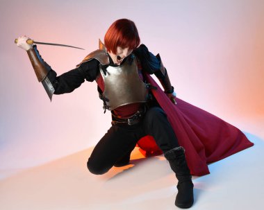 Fantezi savaşçısı kadın modelin portresi, kılıç hançeri silahı, kırmızı peri masalı pelerinli tarihi bir ortaçağ zırhı, güçlü bir fantezi şövalyesi. Stüdyo arka planında izole