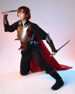 Fantezi savaşçısı kadın modelin portresi, kılıç hançeri silahı, kırmızı peri masalı pelerinli tarihi bir ortaçağ zırhı, güçlü bir fantezi şövalyesi. Stüdyo arka planında izole