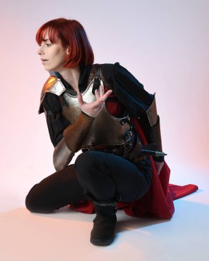 Savaşçı kadın şövalyenin tam boy fantezi portresi, tarihi ortaçağ çelik zırh kostümü giyen bir model, kırmızı peri masalı pelerini. Çömelme pozisyonu, izole stüdyo arka planı.