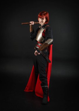 Savaşçı kadın şövalyenin fantezi portresi, tarihi ortaçağ zırhı giymiş bir model, kırmızı peri masalı pelerini. Elinde savaş baltası, izole edilmiş karanlık stüdyo geçmişi var..