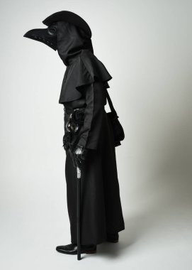 Veba Doktoru Walking Away, Gotik Cadılar Bayramı Karakterinin Uzun Boylu Siluet Portresi Gaga Maskeli, Siyah Pelerin, Beyaz Stüdyo Arkaplanda Yürüyen Sopa, Dramatik Karanlık Kostüm ve Fantezi Korku figürü