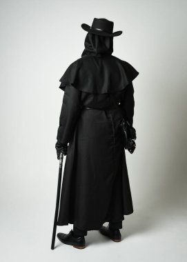 Veba Doktoru Walking Away, Gotik Cadılar Bayramı Karakterinin Uzun Boylu Siluet Portresi Gaga Maskeli, Siyah Pelerin, Beyaz Stüdyo Arkaplanda Yürüyen Sopa, Dramatik Karanlık Kostüm ve Fantezi Korku figürü