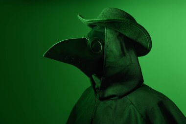 Veba Doktoru Cadılar Bayramı Kostümlü Portre Parlayan Yeşil arka planlı, Gotik Kuş Maskeli Karakter. Siluet profil figürlü Karanlık Fantezi Korku Sahnesi.