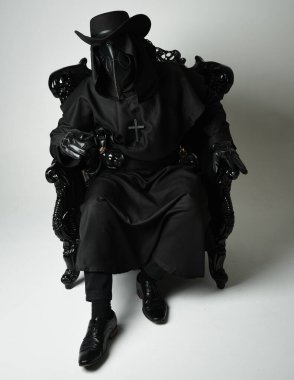 Fenerli Gotik Veba Doktoru, Kara Pelerinli Cadılar Bayramı Karakteri, Kuş Maskeli, kadife taht koltuğunda oturan. Gizemli Fantezi Korku figürünün Stüdyo Portresi