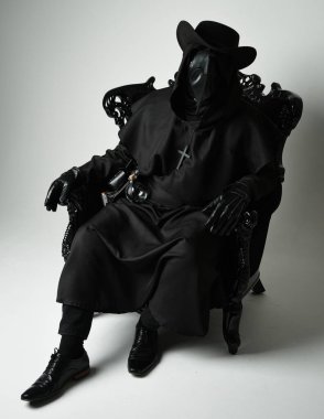 Fenerli Gotik Veba Doktoru, Kara Pelerinli Cadılar Bayramı Karakteri, Kuş Maskeli, kadife taht koltuğunda oturan. Gizemli Fantezi Korku figürünün Stüdyo Portresi