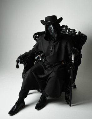 Fenerli Gotik Veba Doktoru, Kara Pelerinli Cadılar Bayramı Karakteri, Kuş Maskeli, kadife taht koltuğunda oturan. Gizemli Fantezi Korku figürünün Stüdyo Portresi