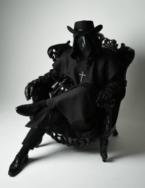 Fenerli Gotik Veba Doktoru, Kara Pelerinli Cadılar Bayramı Karakteri, Kuş Maskeli, kadife taht koltuğunda oturan. Gizemli Fantezi Korku figürünün Stüdyo Portresi