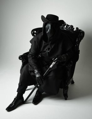 Fenerli Gotik Veba Doktoru, Kara Pelerinli Cadılar Bayramı Karakteri, Kuş Maskeli, kadife taht koltuğunda oturan. Gizemli Fantezi Korku figürünün Stüdyo Portresi