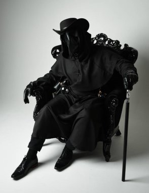 Fenerli Gotik Veba Doktoru, Kara Pelerinli Cadılar Bayramı Karakteri, Kuş Maskeli, kadife taht koltuğunda oturan. Gizemli Fantezi Korku figürünün Stüdyo Portresi