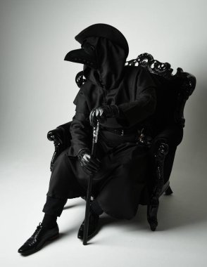 Fenerli Gotik Veba Doktoru, Kara Pelerinli Cadılar Bayramı Karakteri, Kuş Maskeli, kadife taht koltuğunda oturan. Gizemli Fantezi Korku figürünün Stüdyo Portresi