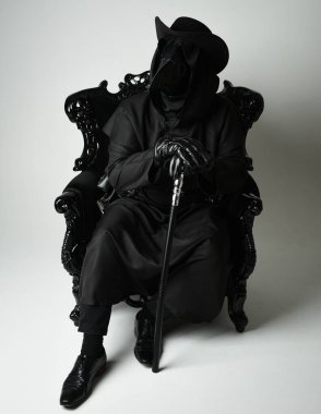 Fenerli Gotik Veba Doktoru, Kara Pelerinli Cadılar Bayramı Karakteri, Kuş Maskeli, kadife taht koltuğunda oturan. Gizemli Fantezi Korku figürünün Stüdyo Portresi