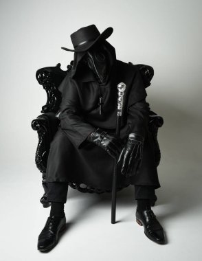 Fenerli Gotik Veba Doktoru, Kara Pelerinli Cadılar Bayramı Karakteri, Kuş Maskeli, kadife taht koltuğunda oturan. Gizemli Fantezi Korku figürünün Stüdyo Portresi