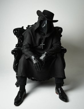 Fenerli Gotik Veba Doktoru, Kara Pelerinli Cadılar Bayramı Karakteri, Kuş Maskeli, kadife taht koltuğunda oturan. Gizemli Fantezi Korku figürünün Stüdyo Portresi