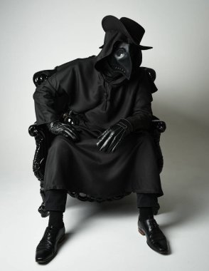 Fenerli Gotik Veba Doktoru, Kara Pelerinli Cadılar Bayramı Karakteri, Kuş Maskeli, kadife taht koltuğunda oturan. Gizemli Fantezi Korku figürünün Stüdyo Portresi