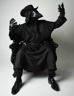 Fenerli Gotik Veba Doktoru, Kara Pelerinli Cadılar Bayramı Karakteri, Kuş Maskeli, kadife taht koltuğunda oturan. Gizemli Fantezi Korku figürünün Stüdyo Portresi