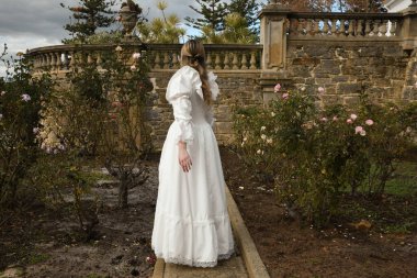 Tarihi beyaz gelinlik giyen güzel sarışın mankenin portresi. Cennetin arka plan figürü, romantik gül bahçesinde yürüyen peri masalı kale bahçesi arka planı