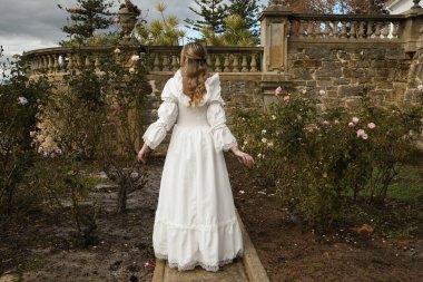 Tarihi beyaz gelinlik giyen güzel sarışın mankenin portresi. Cennetin arka plan figürü, romantik gül bahçesinde yürüyen peri masalı kale bahçesi arka planı