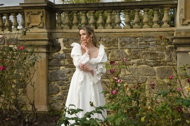 Tarihi fantezi beyaz gelinlik giyen güzel sarışın mankenin portresi. Peri masalı şatosu bahçesinin romantik gül bahçesinde gezinen ruhani figür.