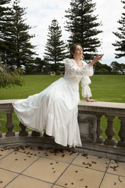 Beyaz fantezi gelinlik giyen sarışın kadın model figürü. Romantik oturma pozu tarihi masal kalesinin merdivenlerinde 