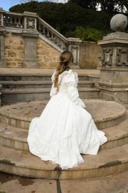 Beyaz fantezi gelinlik giyen sarışın kadın modelin arka plan figürü. Romantik oturma pozu tarihi masal kalesinin merdivenlerine bakıyor. 
