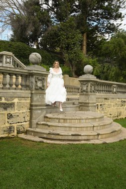 Tarihsel beyaz gelinlik giyen güzel sarışın modelin romantik portresi. Peri masalı şatosunun tarihi merdivenlerinde yürüyen ruhani bir figür..