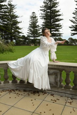 Beyaz fantezi gelinlik giyen sarışın kadın model figürü. Romantik oturma pozu tarihi masal kalesinin merdivenlerinde 