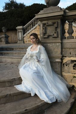 Fantezi beyaz balo elbisesi ve kelebek maskesi giyen güzel sarışın mankenin portresi. Romantik figür tarihi masal kalesinde poz veriyor. 