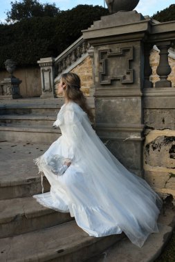 Fantezi beyaz balo elbisesi ve kelebek maskesi giyen güzel sarışın mankenin portresi. Romantik figür tarihi masal kalesinde poz veriyor. 