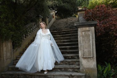 Tarihi beyaz gelinlik ve fantezi pelerin giyen güzel sarışın mankenin portresi. Peri masalı şatosunun tarihi merdivenlerinde yürüyen ruhani bir figür..