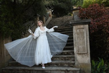 Tarihi beyaz gelinlik ve fantezi pelerin giyen güzel sarışın mankenin portresi. Peri masalı şatosunun tarihi merdivenlerinde yürüyen ruhani bir figür..