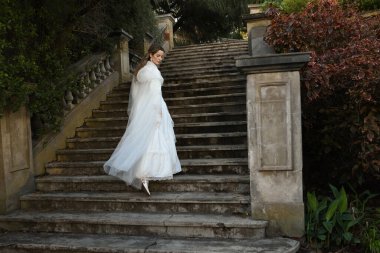 Tarihi beyaz gelinlik ve fantezi pelerin giyen güzel sarışın mankenin portresi. Peri masalı şatosunun tarihi merdivenlerinde yürüyen ruhani bir figür..