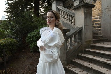 Tarihsel beyaz gelinlik giyen güzel sarışın modelin romantik portresi. Peri masalı şatosunun tarihi merdivenlerinde yürüyen ruhani bir figür..