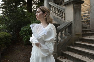 Tarihsel beyaz gelinlik giyen güzel sarışın modelin romantik portresi. Peri masalı şatosunun tarihi merdivenlerinde yürüyen ruhani bir figür..