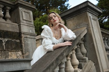 Fantezi beyaz balo elbisesi giyen güzel sarışın mankenin portresi. Romantik figür, tarihi masal kalesinin balkonunda poz veriyor. 