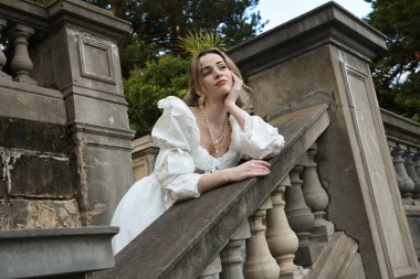 Fantezi beyaz balo elbisesi giyen güzel sarışın mankenin portresi. Romantik figür, tarihi masal kalesinin balkonunda poz veriyor. 