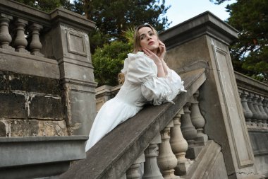 Fantezi beyaz balo elbisesi giyen güzel sarışın mankenin portresi. Romantik figür, tarihi masal kalesinin balkonunda poz veriyor. 