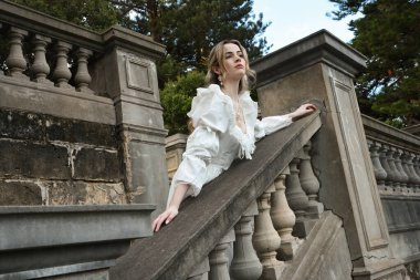 Fantezi beyaz balo elbisesi giyen güzel sarışın mankenin portresi. Romantik figür, tarihi masal kalesinin balkonunda poz veriyor. 