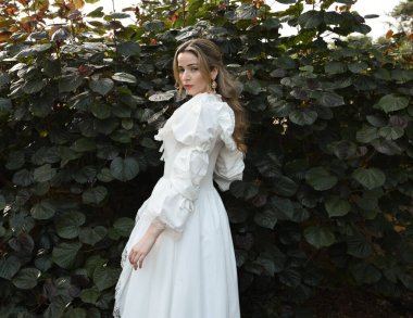 Tarihsel fantezi beyaz gelinlik giyen güzel sarışın mankenin portresi. El hareketleriyle doğal bitki arka planına poz veriyor..