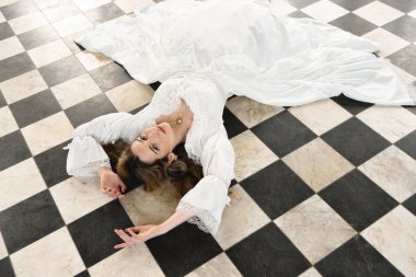 Tarihi fantezi beyaz gelinlik giyen güzel sarışın mankenin portresi. El hareketleriyle yere uzanmış. siyah ve beyaz dama tahtası arkaplanı.