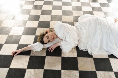 Tarihi fantezi beyaz gelinlik giyen güzel sarışın mankenin portresi. El hareketleriyle yere uzanmış. siyah ve beyaz dama tahtası arkaplanı.