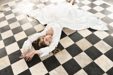 Tarihi fantezi beyaz gelinlik giyen güzel sarışın mankenin portresi. El hareketleriyle yere uzanmış. siyah ve beyaz dama tahtası arkaplanı.