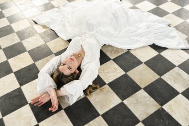 Tarihi fantezi beyaz gelinlik giyen güzel sarışın mankenin portresi. El hareketleriyle yere uzanmış. siyah ve beyaz dama tahtası arkaplanı.