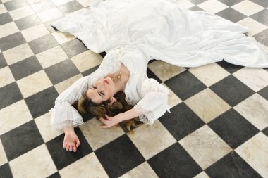 Tarihi fantezi beyaz gelinlik giyen güzel sarışın mankenin portresi. El hareketleriyle yere uzanmış. siyah ve beyaz dama tahtası arkaplanı.