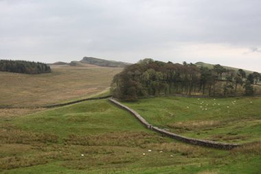 Antik Roma İmparatorluğu anıtı Hadrians Duvarı 'nın engebeli İskoç dağlık kırsalındaki sinematik manzarası rüzgarlı bir bozkıra çarpan tarihi bir dönüm noktası.