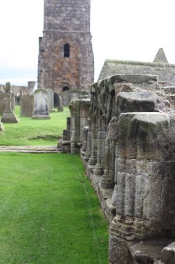 İskoçya 'daki Aziz Andrews Manastırı' nın atmosferik manzarası, dağılan gotik mimari, bulutlu kıyı gökyüzünün altında perili bir mezarlıkla çevrili..
