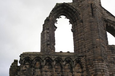 İskoçya 'daki Aziz Andrews Manastırı' nın atmosferik manzarası, dağılan gotik mimari, bulutlu kıyı gökyüzünün altında perili bir mezarlıkla çevrili..