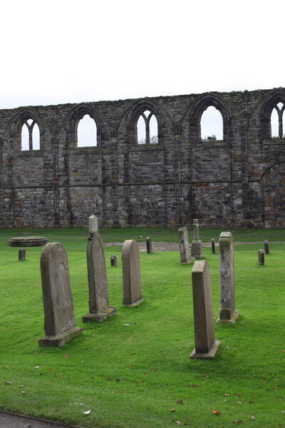 Atmospheric landscape of St Andrews Abbey in Scotland, crumbling gothic architecture surrounded by a haunting graveyard beneath overcast coastal skies.